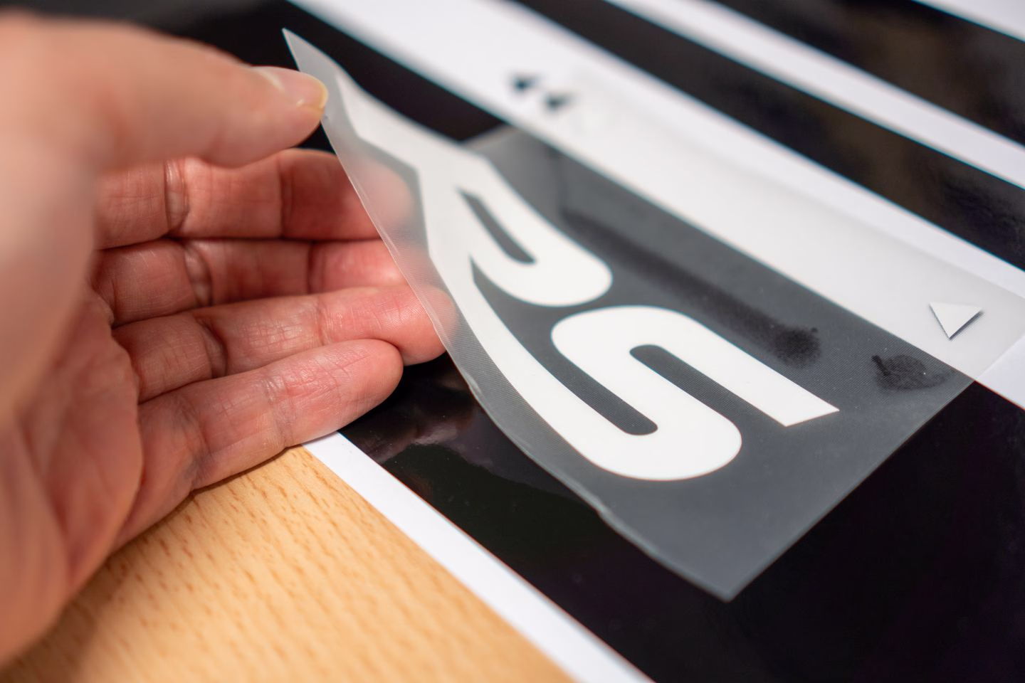 Hands applying transfer film to cut vinyl lettering — Source Select.