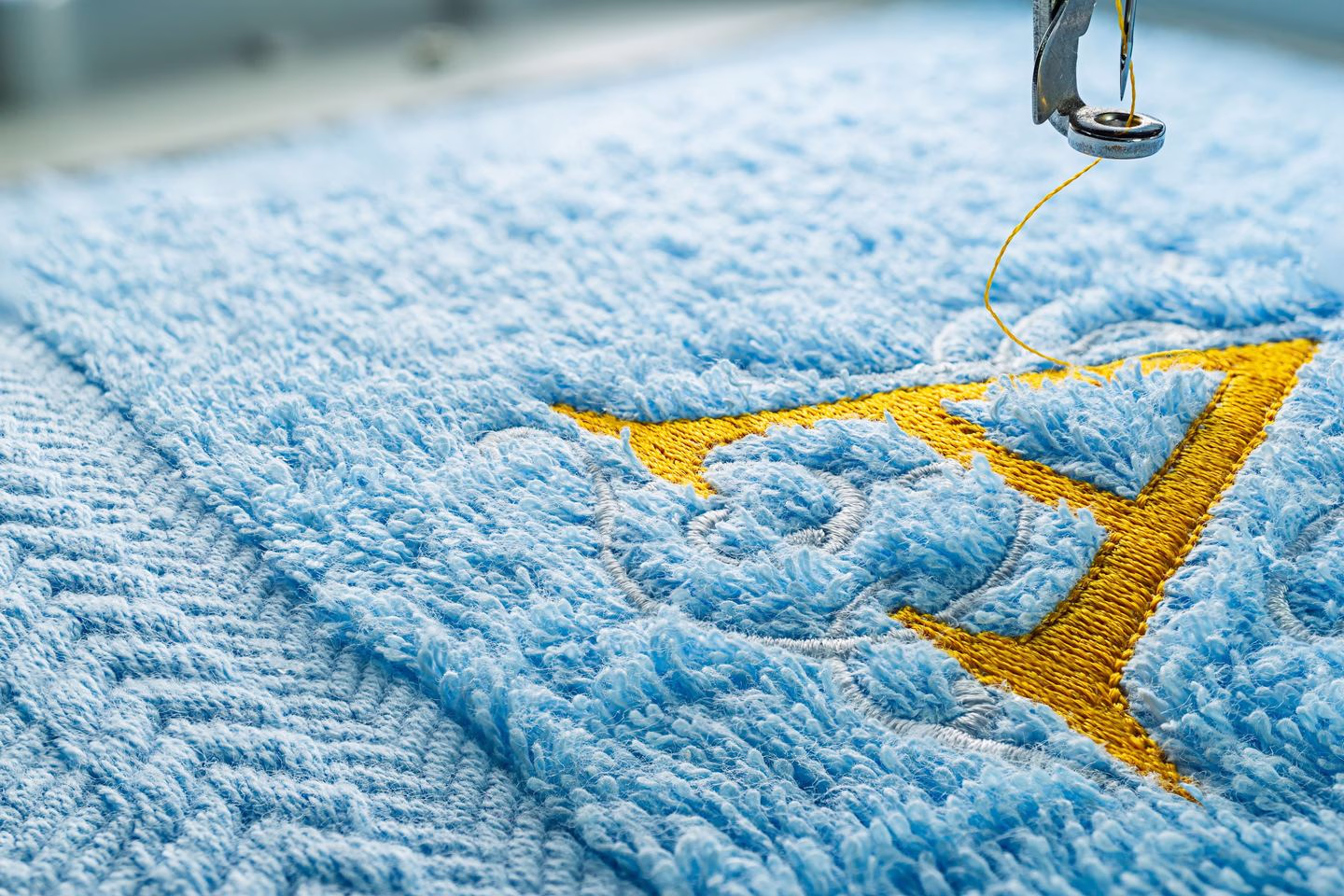 Yellow monogram stitched into blue fabric — Source Select.