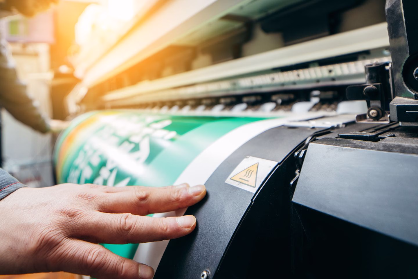 Hands operating a large-format printer — Source Select.