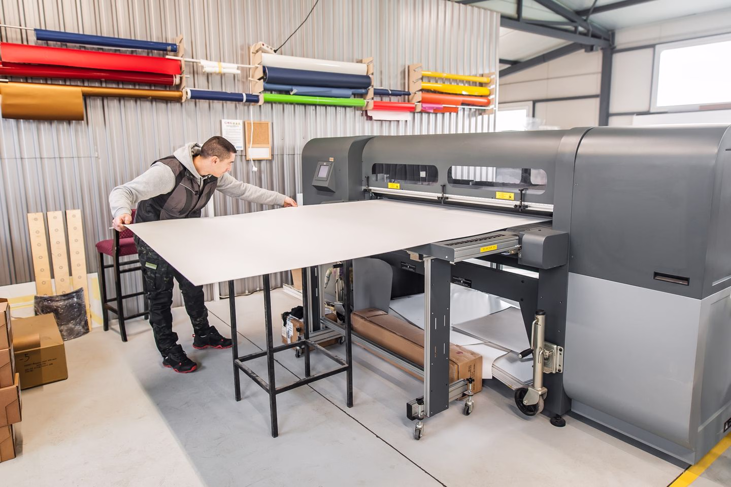 Operator handling printed sheets at a large-format printer — Source Select.