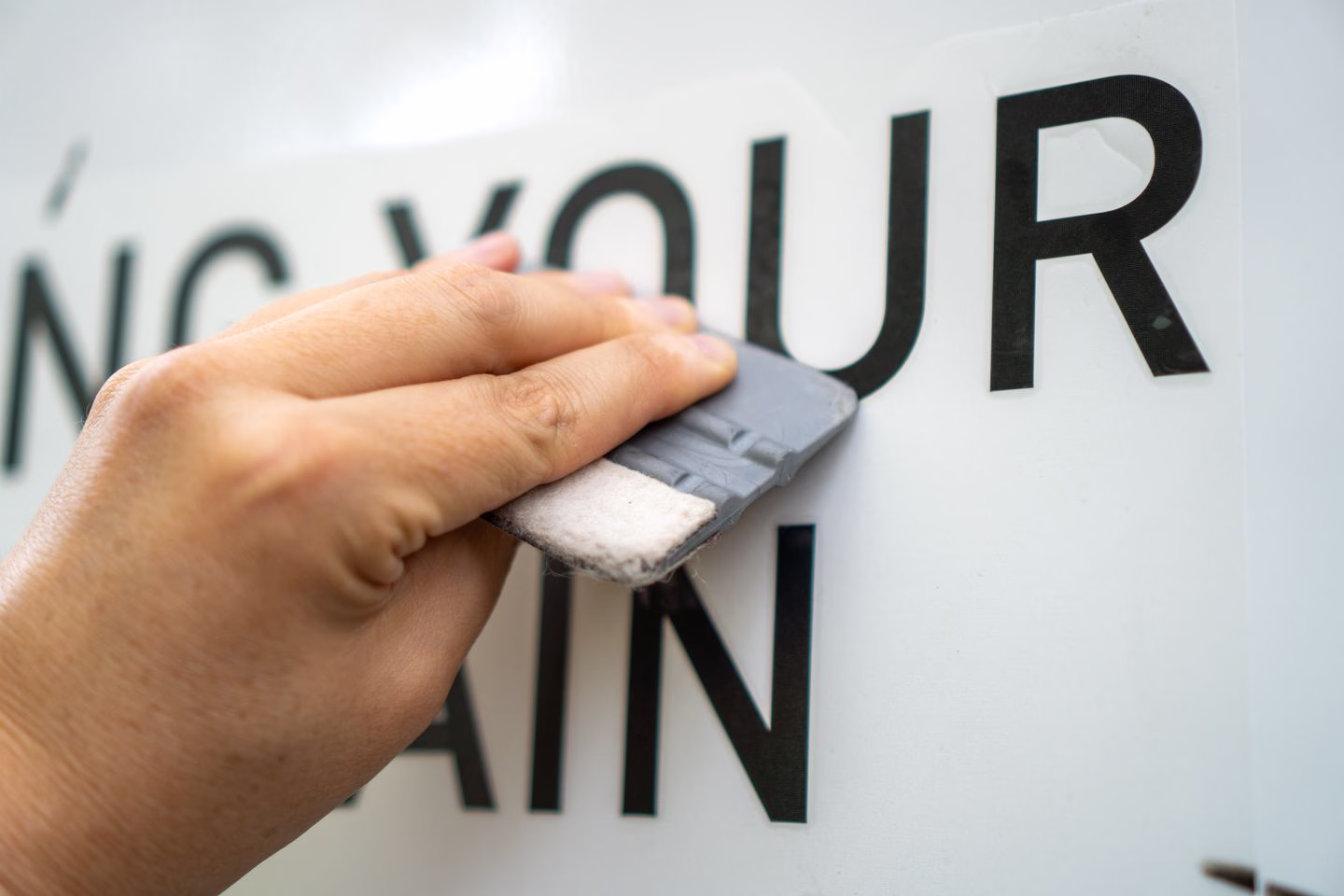 Hands smoothing vinyl lettering with a squeegee — Source Select.